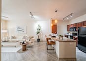 Thumbnail 20 of 35 - A modern kitchen and living room with a white couch, wooden coffee table, and a potted plant.