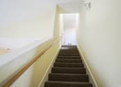 Thumbnail 6 of 16 - A staircase with a brown carpeted runner and white walls.