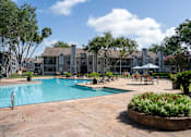Thumbnail 50 of 68 - A pool surrounded by a patio and trees with a building in the background.