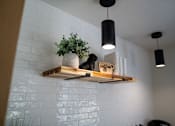 Thumbnail 68 of 68 - A white brick wall with a wooden shelf holding a potted plant, a black cat, and a wooden sign.