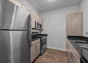 Thumbnail 15 of 17 - A kitchen with a stainless steel refrigerator, microwave, oven, and black countertops.