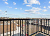Thumbnail 27 of 42 - A balcony with a black railing overlooks a parking lot and a road.