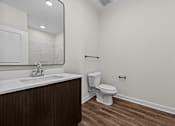 Thumbnail 32 of 42 - A white toilet sits in a bathroom with a wooden vanity and marble counter.