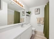 Thumbnail 25 of 27 - a bathroom with a white sink and a toilet and a green shower curtain