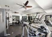 Thumbnail 8 of 27 - a gym with cardio equipment and a ceiling fan