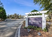 Thumbnail 1 of 39 - A sign for 10X Trellis by Gardone Capital stands in front of a tree-lined street.