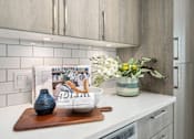 Thumbnail 36 of 47 - A kitchen counter with a bowl, vase, and magazine on it.