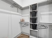 Thumbnail 11 of 34 - A white closet with clothes hanging and baskets on shelves.