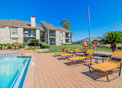 Thumbnail 56 of 61 - A poolside area with chairs and a building in the background.