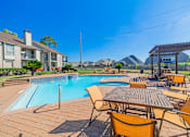 Thumbnail 55 of 61 - A poolside table and chairs are set up in front of a swimming pool.