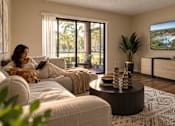 Thumbnail 5 of 52 - A woman is sitting on a couch with a dog, looking at a television screen showing a scenic view.