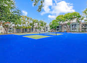 Thumbnail 44 of 51 - A tennis court surrounded by trees and buildings.