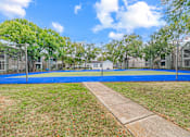 Thumbnail 41 of 51 - A blue tennis court surrounded by trees and a fence.