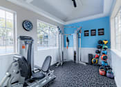 Thumbnail 24 of 51 - A gym room with a rowing machine, weights, and a clock on the wall.