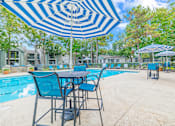 Thumbnail 33 of 51 - A blue and white striped umbrella shades a table and chairs by a pool.