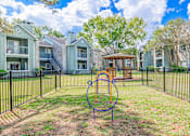 Thumbnail 39 of 51 - A playground with a blue and orange ring structure in the foreground and apartment buildings in the background.