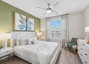 Thumbnail 20 of 26 - A bedroom with a large bed, a ceiling fan, and a window with a view of a building outside.