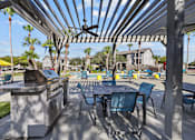 Thumbnail 10 of 20 - A patio with a grill and chairs under a pergola.