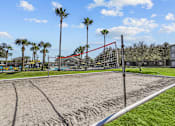 Thumbnail 17 of 20 - A sand volleyball court with a red net and a blue sky in the background.