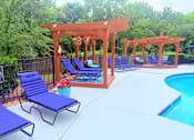 Thumbnail 6 of 47 - A poolside area with blue lounge chairs and a wooden pergola.