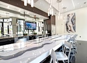 Thumbnail 19 of 20 - A long white marble bar with white chairs and a TV on the wall.