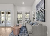 Thumbnail 7 of 30 - A living room with a grey couch, a wooden table, and a painting on the wall.