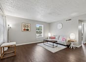 Thumbnail 3 of 22 - A living room with a white couch, a wooden coffee table, and a painting on the wall.