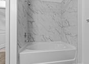 Thumbnail 31 of 41 - A white bathtub with a marble wall behind it.