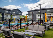 Thumbnail 17 of 25 - A poolside area with chairs, a sofa, and umbrellas in front of a building.
