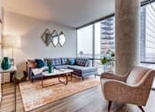 Thumbnail 6 of 19 - A living room with a grey sofa, a brown armchair, and a white coffee table.
