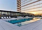 Thumbnail 14 of 19 - A large swimming pool is surrounded by lounge chairs in front of a modern building.