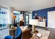 Thumbnail 8 of 26 - A blue chair sits in a living room with a white couch and a table with a lamp on it.