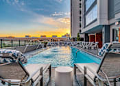 Thumbnail 17 of 26 - A pool area with lounge chairs and a view of the city skyline at sunset.