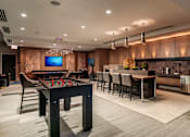 Thumbnail 16 of 26 - A modern room with a foosball table, bar stools, and a television.