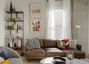 Thumbnail 2 of 16 - A living room with a brown couch and a glass table.