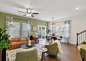 Thumbnail 7 of 16 - A living room with a brown leather couch, a green armchair, and a round table with a candle on it.