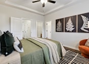 Thumbnail 11 of 16 - A bedroom with a bed, pillows, a blanket, a chair, and a ceiling fan.