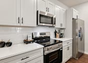 Thumbnail 6 of 16 - A modern kitchen with white cabinets and stainless steel appliances.