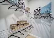 Thumbnail 12 of 26 - A white closet with clothes hanging and shelves with baskets.