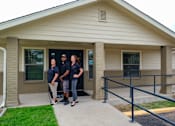 Thumbnail 22 of 23 - Four people in black shirts stand in front of a building.