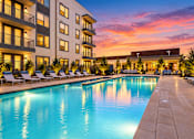 Thumbnail 9 of 30 - A large swimming pool is surrounded by lounge chairs in front of a building.