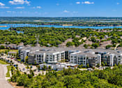 Thumbnail 29 of 30 - A large apartment complex is surrounded by trees and overlooks a large body of water.