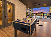 Thumbnail 13 of 30 - A foosball table is in the middle of a room with a pool table and a bar in the background.