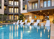 Thumbnail 10 of 30 - A swimming pool in front of a building with white chairs around it.