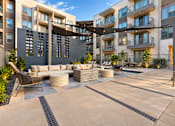 Thumbnail 8 of 30 - A modern outdoor seating area with a large table and chairs is surrounded by apartment buildings.