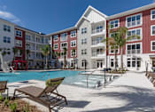 Thumbnail 37 of 48 - A pool area with lounge chairs and a fountain in front of apartment buildings.