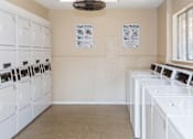Thumbnail 19 of 24 - A laundry room with a row of washers and dryers.