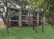 Thumbnail 22 of 24 - Apartment complex with green grass and trees in front.
