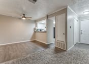 Thumbnail 9 of 20 - an empty living room with a ceiling fan and a kitchen in the background