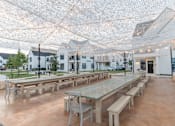 Thumbnail 26 of 30 - A large outdoor dining area with tables and benches under a net of lights.